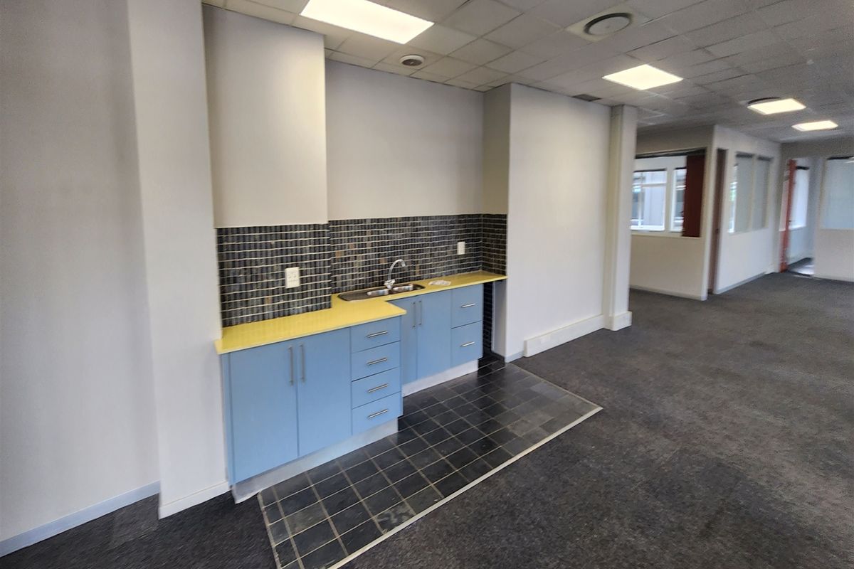 A functional office kitchenette featuring blue cabinetry, a stainless steel sink, and a tiled splashback, set within an open-plan office environment.