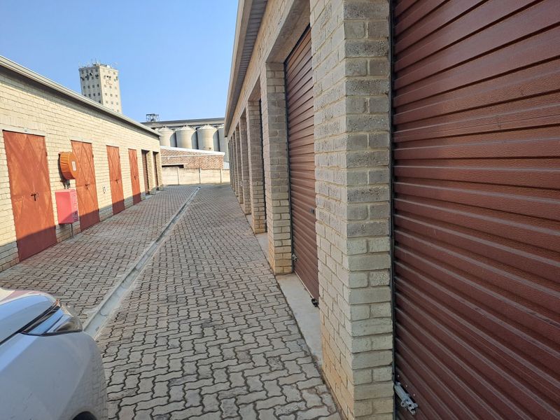 A row of industrial storage garages featuring brick construction, roller shutter doors, and a paved access driveway.
