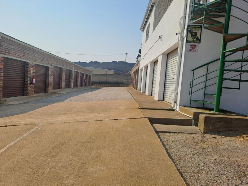 Industrial property exterior featuring multiple roller shutter storage units, concrete driveway access, and an external metal staircase leading to the upper level.
