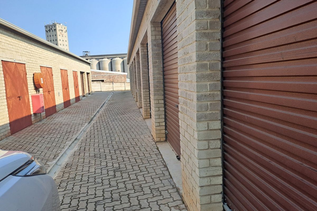 A row of industrial storage garages featuring brick construction, roller shutter doors, and a paved access driveway.