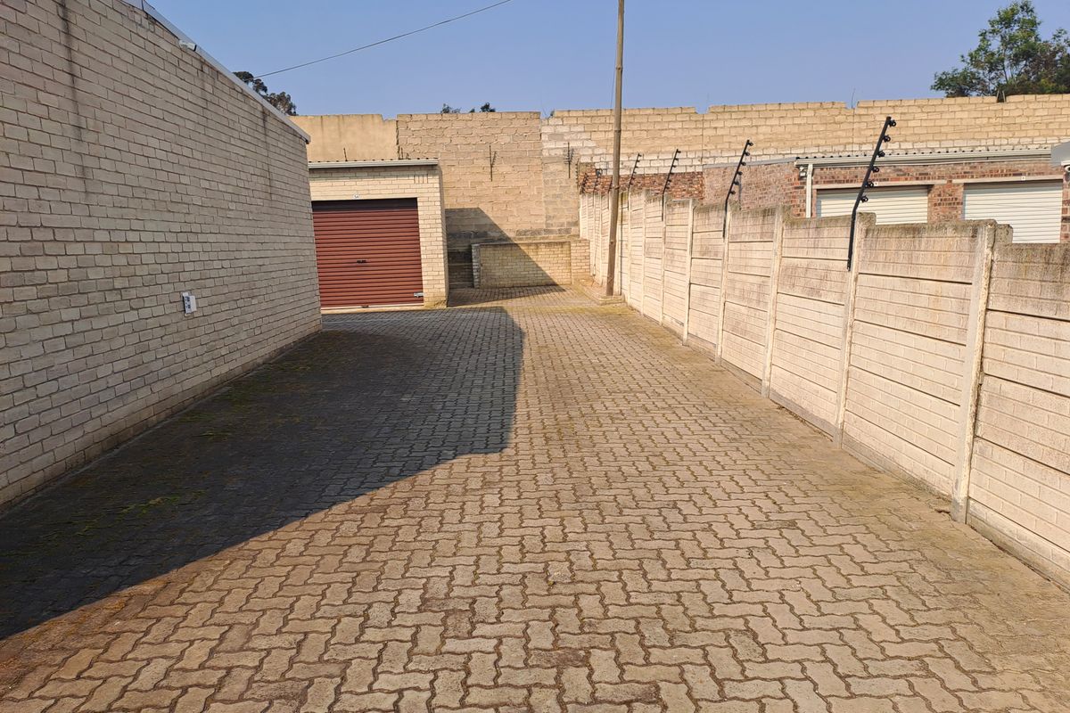 A paved industrial driveway area featuring brick boundary walls with electric fencing and a secure roller shutter garage door.