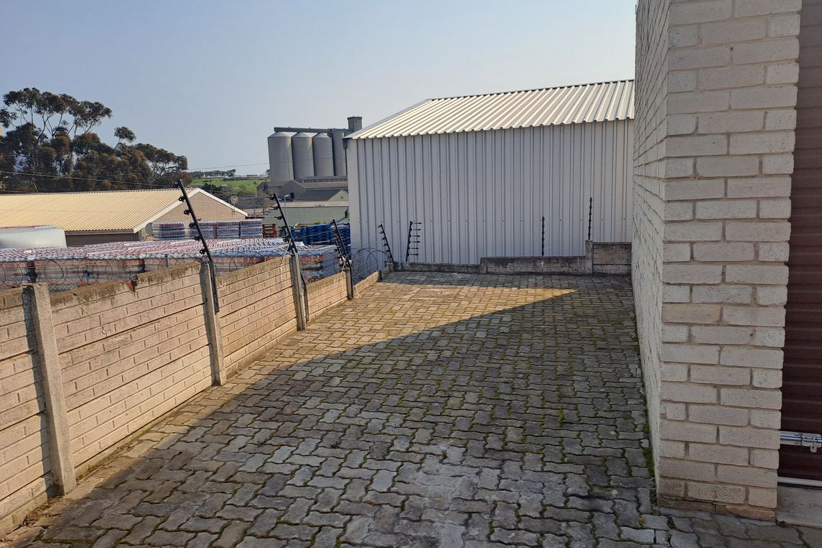 An industrial rear yard area featuring paved surfacing, perimeter precast concrete walling with electric fencing, and access to a metal-clad industrial structure.