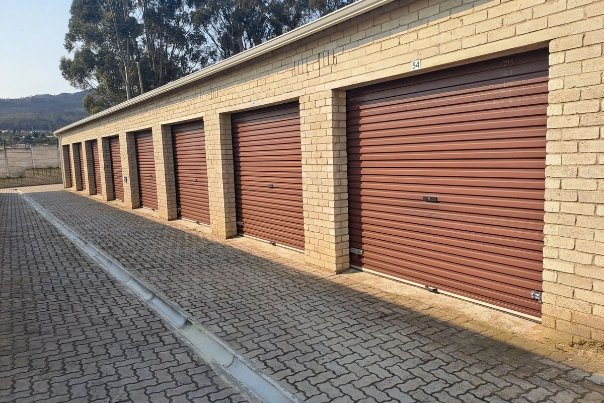 A row of industrial-style storage garages featuring brown roller shutter doors and a paved exterior driveway.