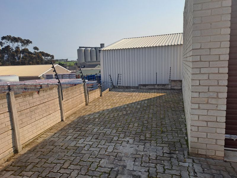 An industrial rear yard area featuring paved surfacing, perimeter precast concrete walling with electric fencing, and access to a metal-clad industrial structure.