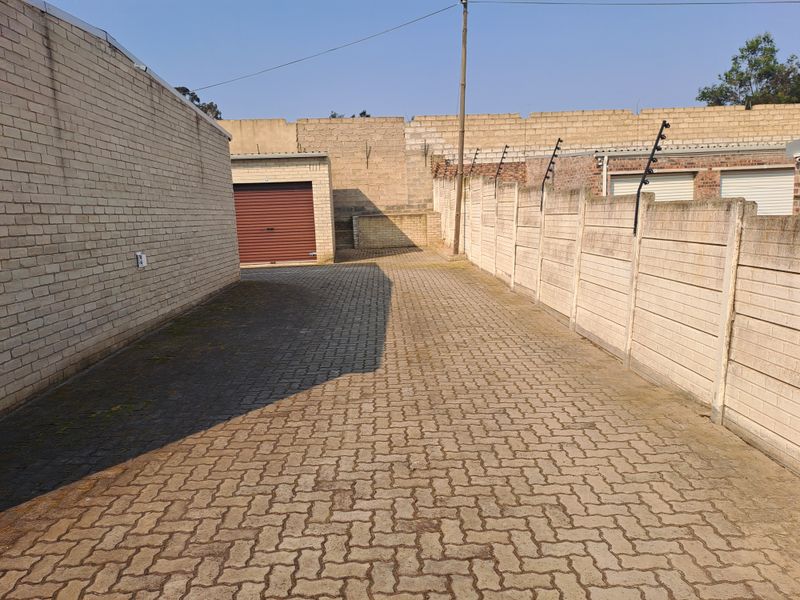 A paved industrial driveway area featuring brick boundary walls with electric fencing and a secure roller shutter garage door.