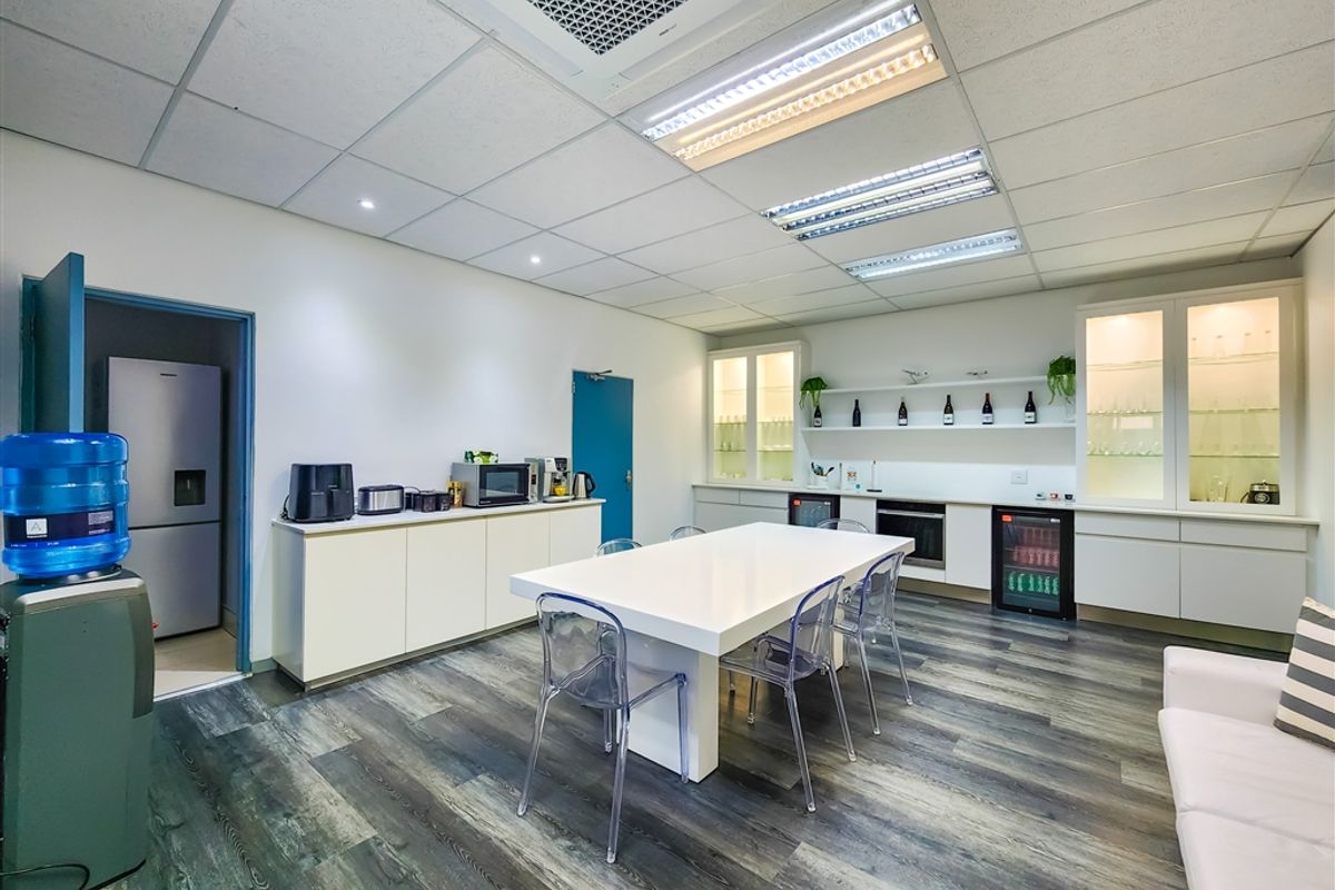 Modern office kitchenette and break area featuring built-in cabinetry, integrated appliances, recessed ceiling lighting, and durable wood-look flooring.