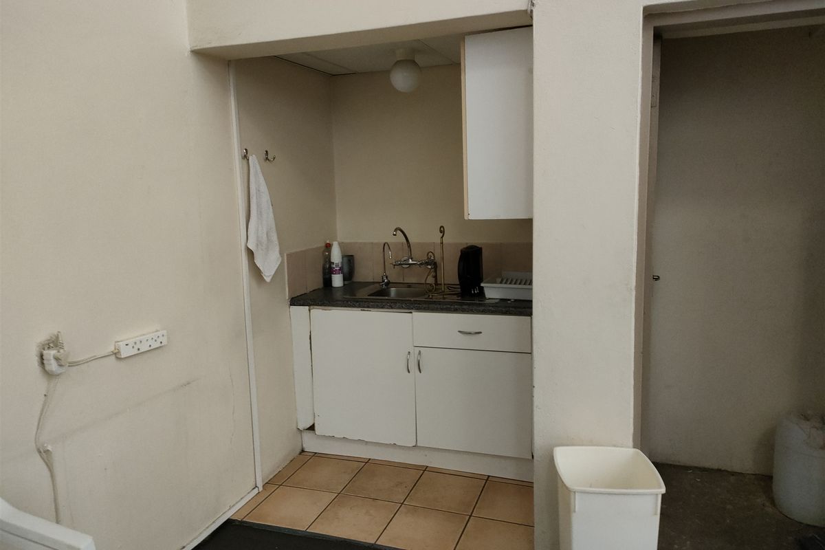 A compact kitchenette area featuring basic cabinetry, a stainless steel sink, and tiled flooring, suitable for a small office or industrial utility space.