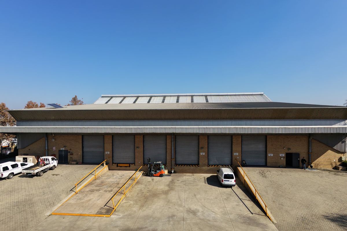 Aerial view of an industrial warehouse facility featuring multiple roller shutter doors, loading ramps, and a paved yard area.