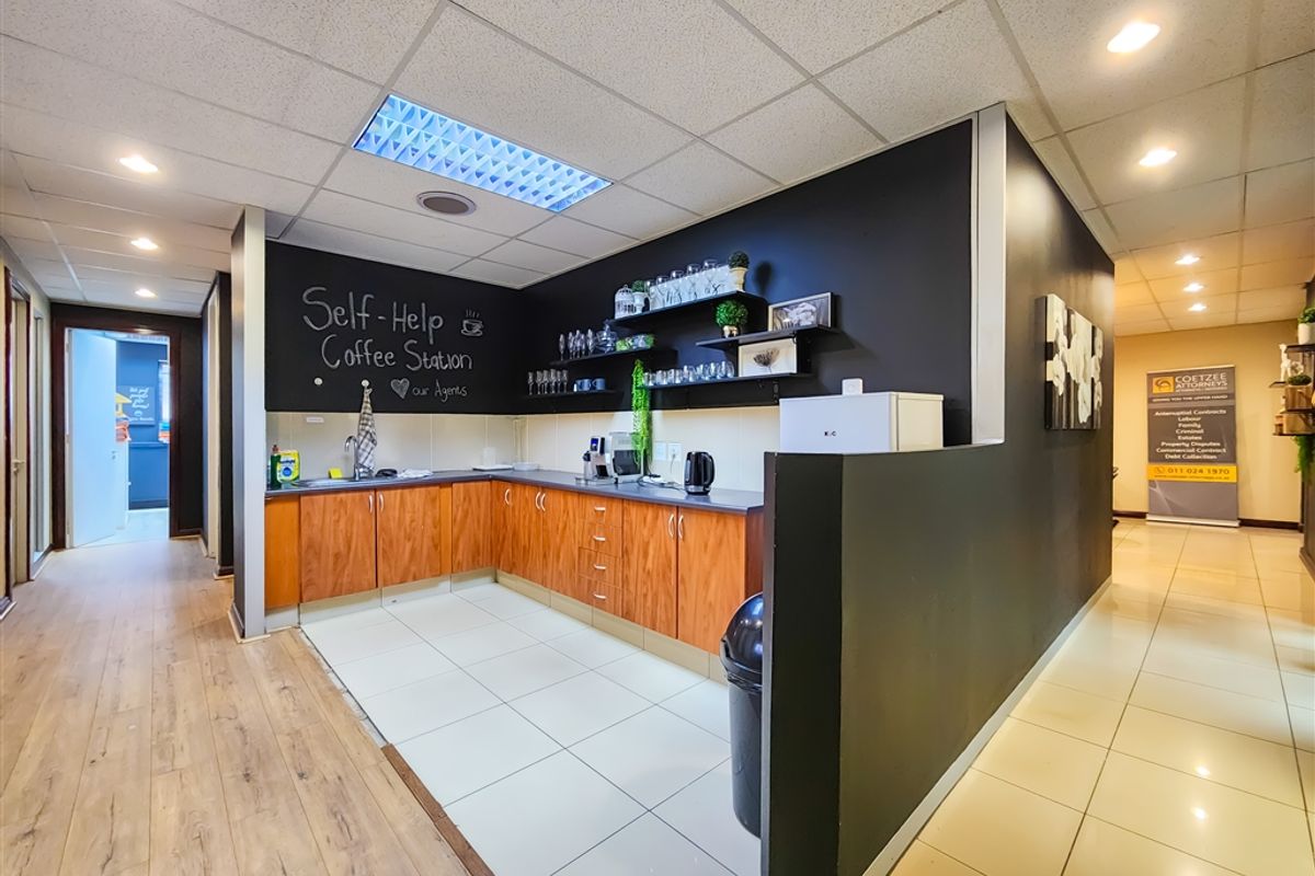 A functional office kitchenette featuring wood-finish cabinetry, a stainless steel sink, and a dedicated coffee station area with black accent walls.
