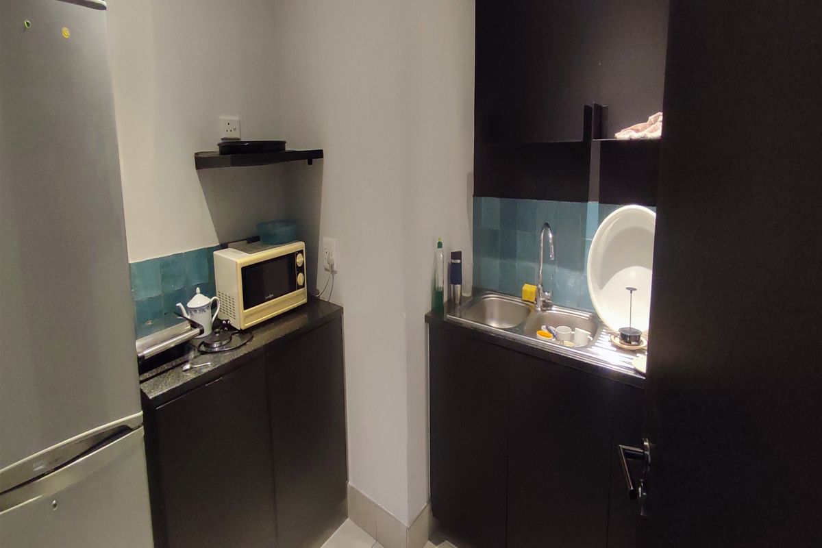 A compact kitchenette area featuring dark cabinetry, a stainless steel sink, and tiled splashbacks, suitable for office staff use.