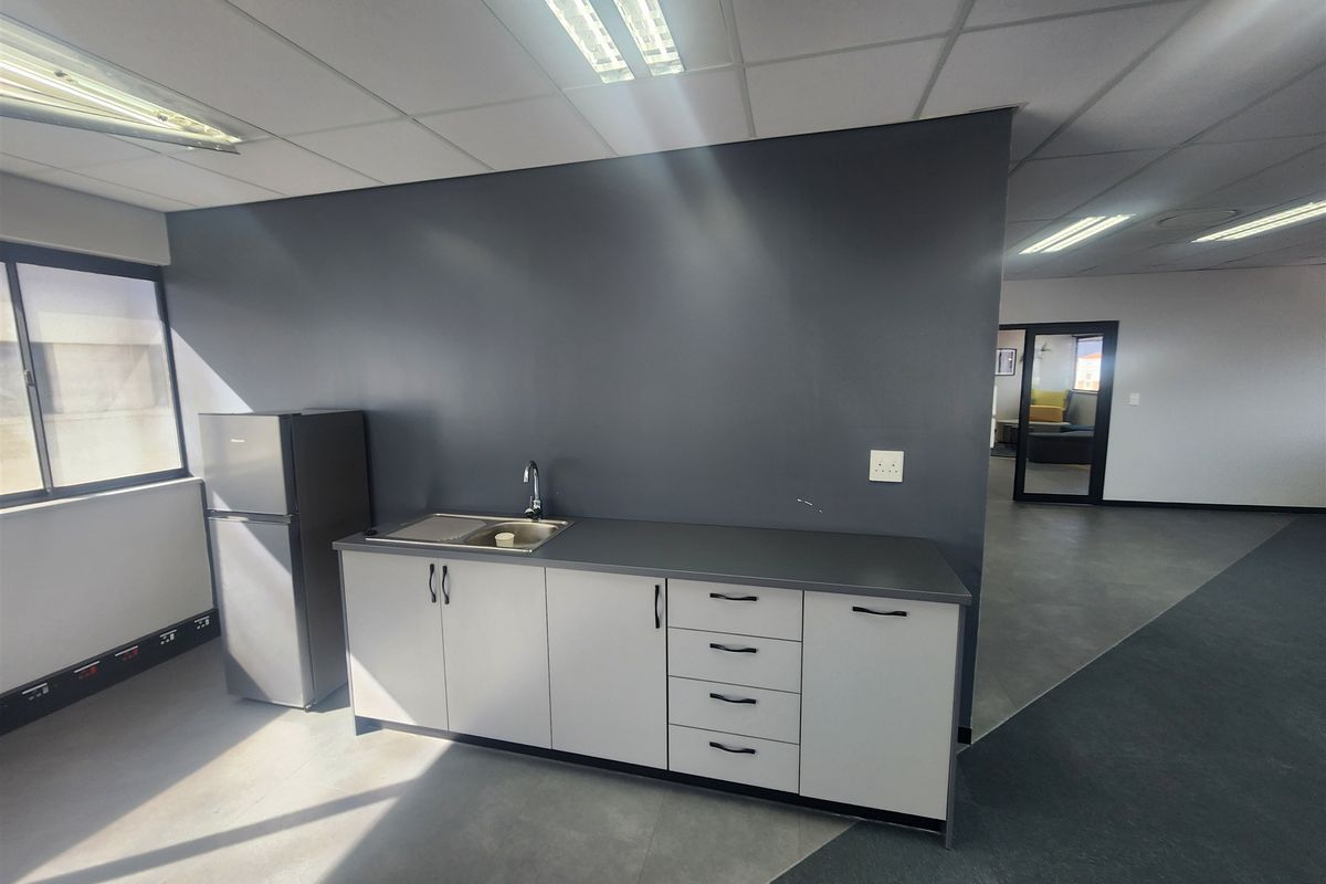 A functional office kitchenette featuring built-in cabinetry, a stainless steel sink, and a dark grey accent wall in an open-plan office environment.