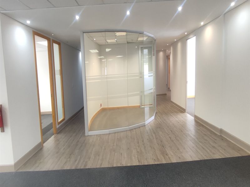A bright, modern office space featuring a curved glass partition wall, recessed ceiling lighting, and durable laminate flooring throughout the open area.