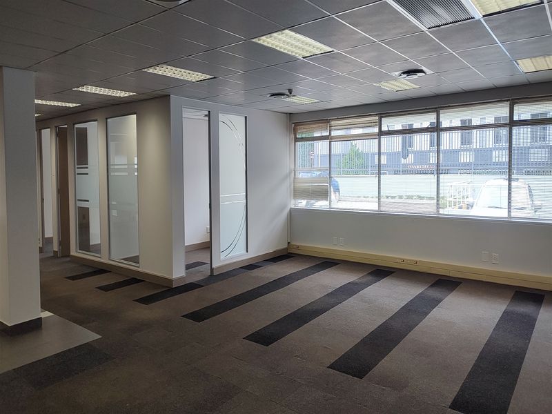 An open-plan office space featuring suspended ceilings, recessed lighting, glass partitions, and large windows with blinds, providing a bright and professional work environment.