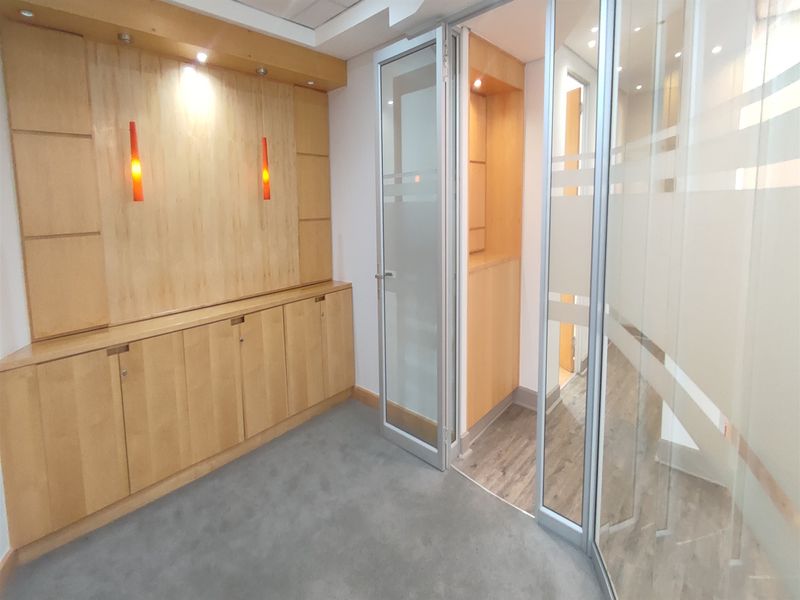 A professional office space featuring built-in wooden cabinetry, glass partition walls, and a combination of carpet and laminate flooring.