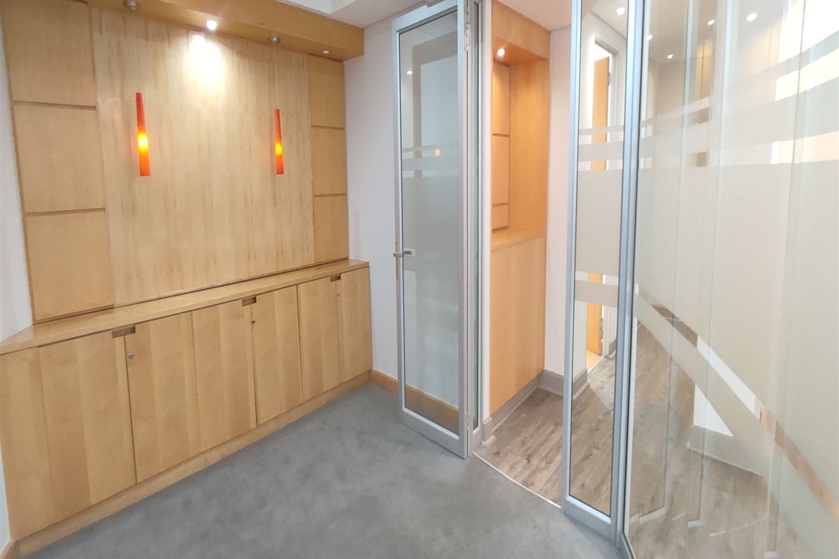A professional office space featuring built-in wooden cabinetry, glass partition walls, and a combination of carpet and laminate flooring.