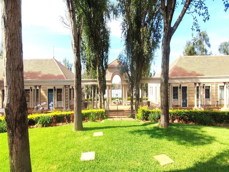A well-maintained office complex exterior featuring symmetrical buildings with tiled roofs, stone columns, and a central landscaped courtyard with an archway.