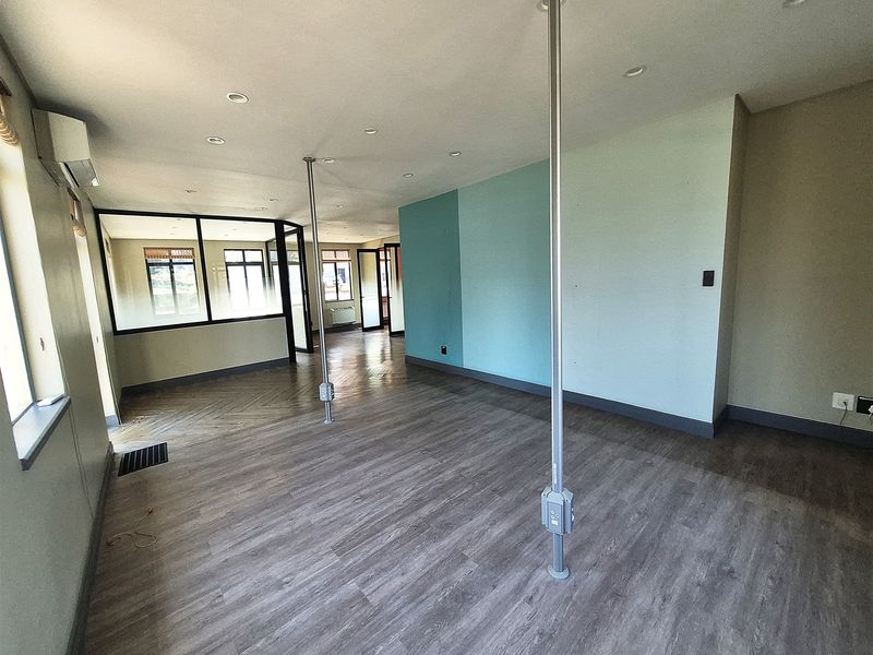 Spacious open-plan office area featuring laminate flooring, recessed lighting, glass partitions, and integrated electrical service poles.