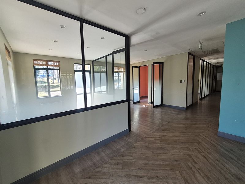 Modern vacant office space featuring glass partitions, herringbone flooring, and recessed lighting, offering a clean and professional environment for business operations.