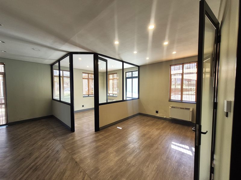A bright, modern office space featuring laminate flooring, recessed lighting, and a glass-partitioned private office area with an integrated HVAC unit.