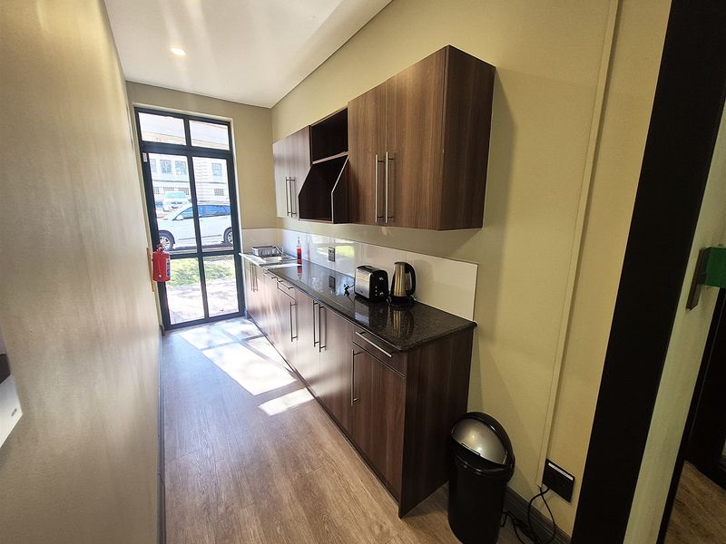 A compact office kitchenette featuring modern dark wood cabinetry, granite countertops, and a stainless steel sink with direct access to the exterior.
