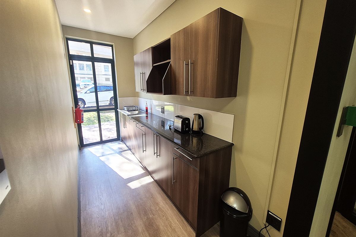 A compact office kitchenette featuring modern dark wood cabinetry, granite countertops, and a stainless steel sink with direct access to the exterior.
