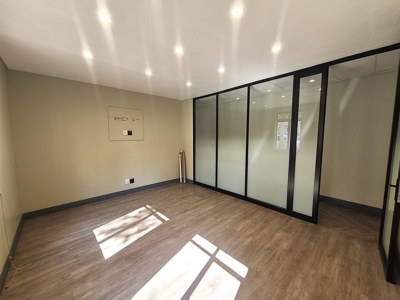 A bright, modern office space featuring laminate flooring, recessed downlights, and a sleek glass partition wall, providing a clean and professional work environment.