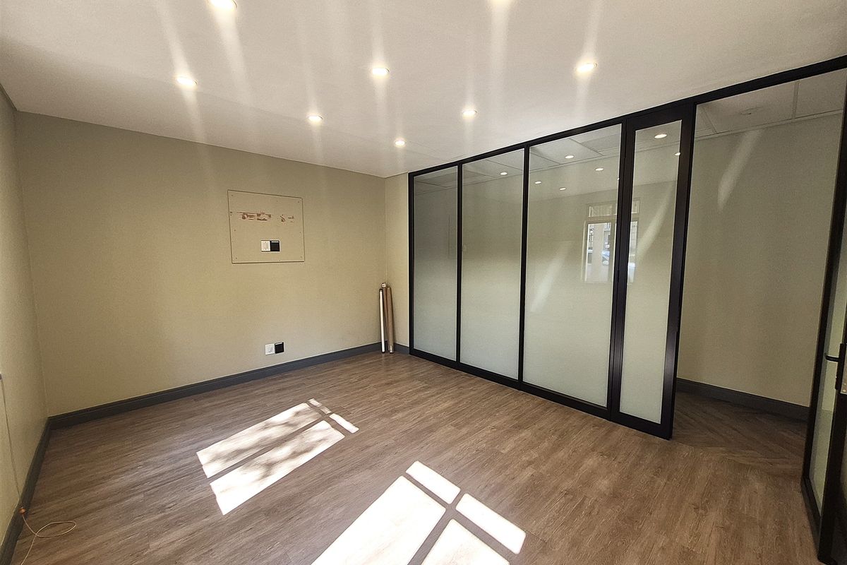 A bright, modern office space featuring laminate flooring, recessed downlights, and a sleek glass partition wall, providing a clean and professional work environment.