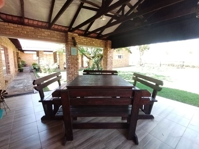 A spacious covered patio featuring exposed timber roof trusses, facebrick pillars, and tiled flooring, overlooking the garden area.