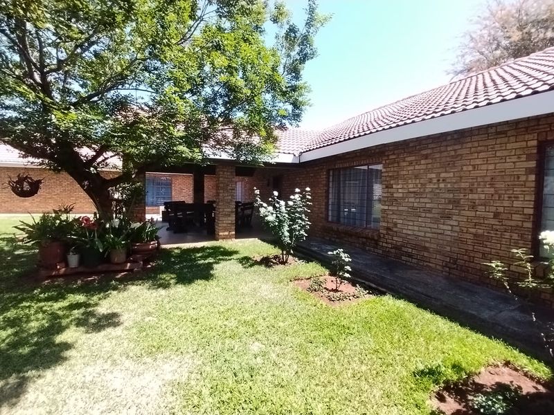 A view of the rear exterior featuring a brick facade, tiled roof, and a covered patio area overlooking a well-maintained garden.