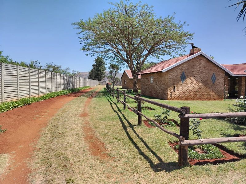 A view of the farm property featuring face brick buildings, a tiled roof, and established garden areas enclosed by timber and concrete fencing.