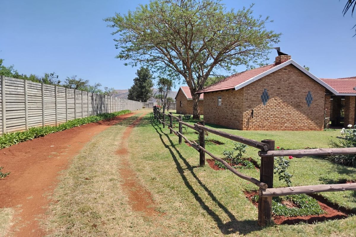 A view of the farm property featuring face brick buildings, a tiled roof, and established garden areas enclosed by timber and concrete fencing.