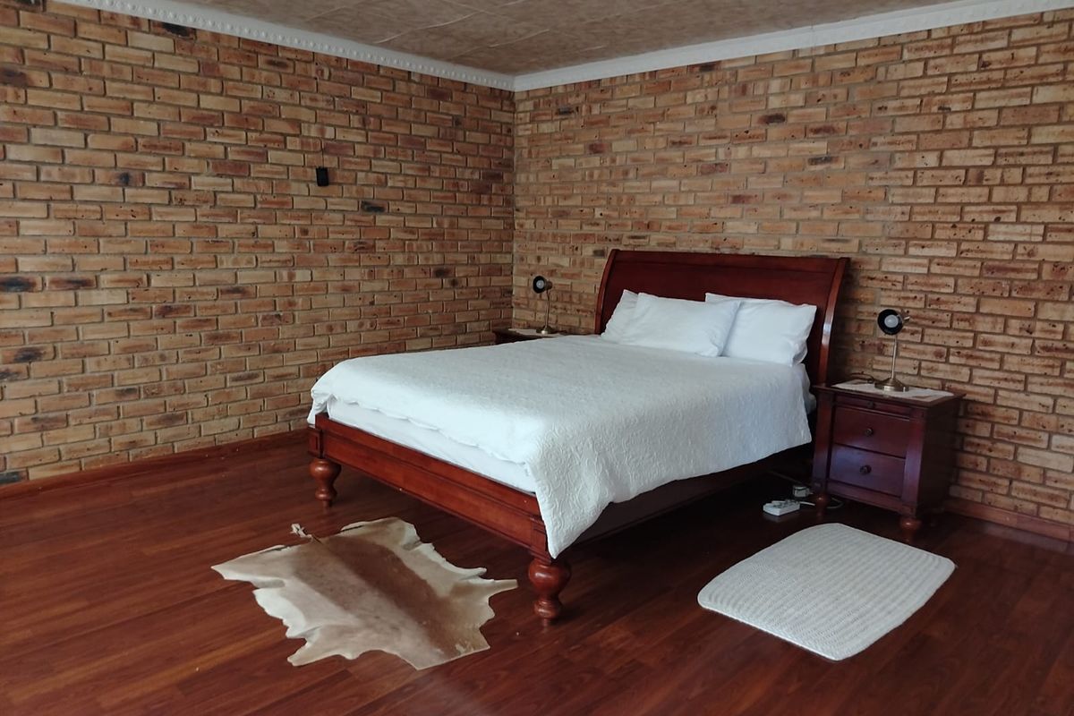 Spacious bedroom featuring rustic exposed brick walls, warm laminate flooring, and a classic coved ceiling finish.