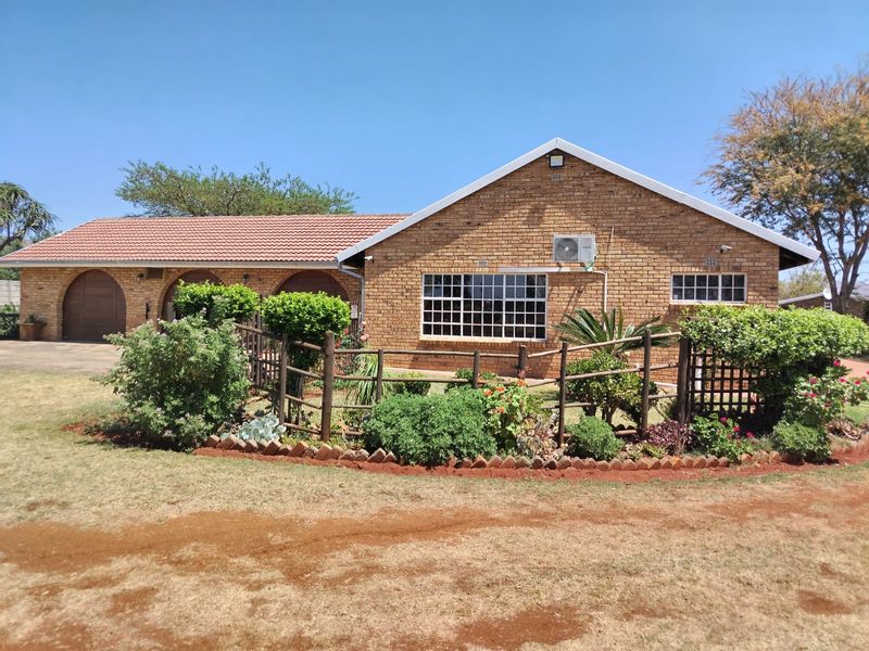 Front view of a face brick farm-style residence featuring a tiled roof, arched garage access, and established garden landscaping with timber fencing.