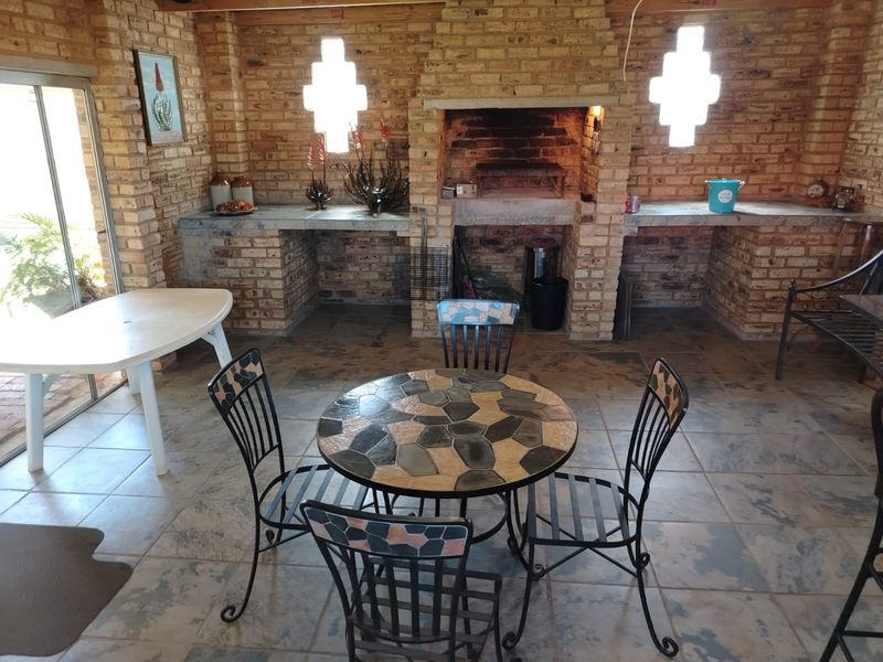 Covered patio area featuring a large built-in brick braai, concrete prep counters, and tiled flooring, providing a functional outdoor entertainment space.