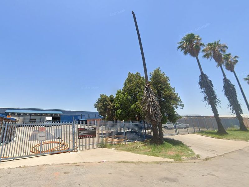 Front view of an industrial property featuring a secure gated entrance, guard house, and warehouse facility with concrete driveway access.