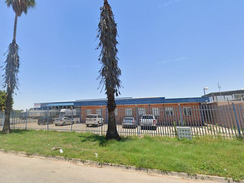 Front exterior view of an industrial property featuring a brick facade, metal roofing, and secure perimeter fencing.