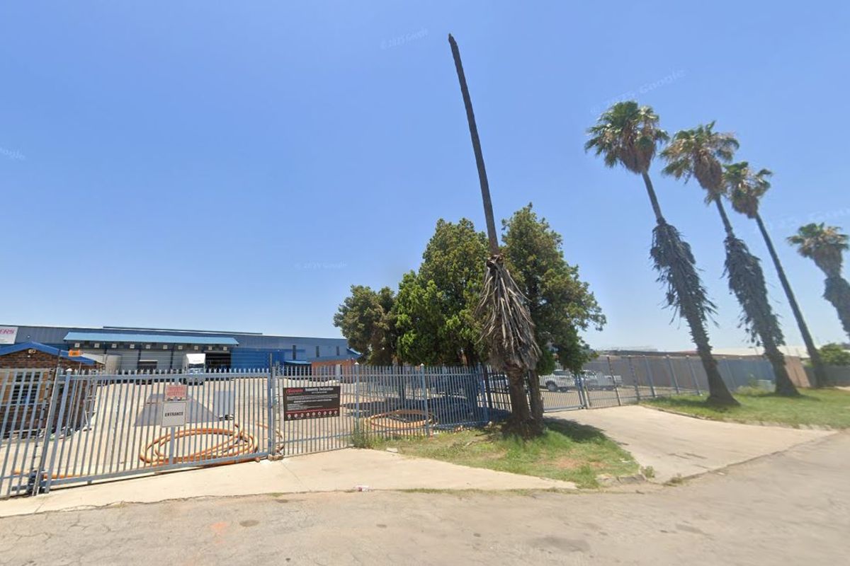 Front view of an industrial property featuring a secure gated entrance, guard house, and warehouse facility with concrete driveway access.
