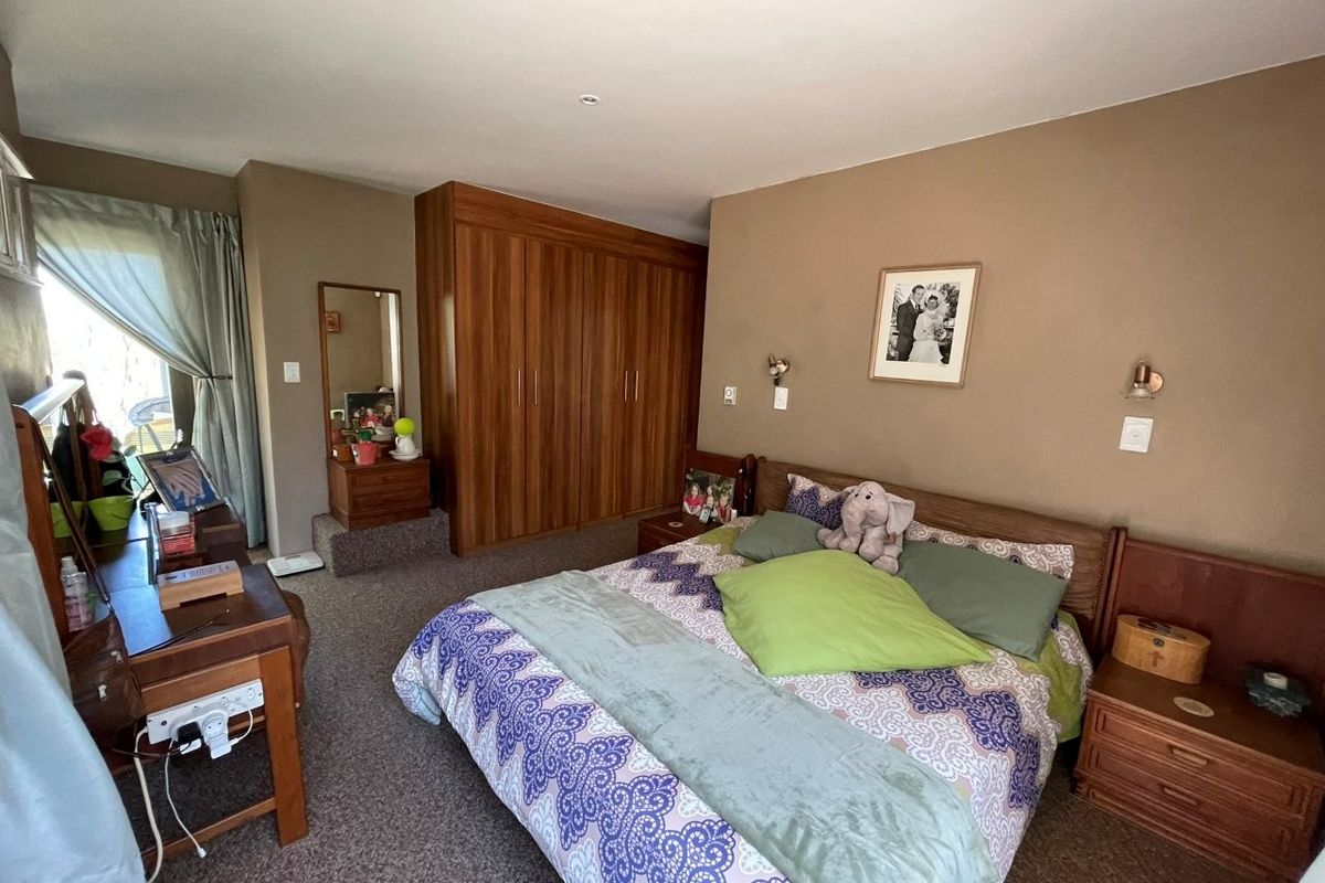 A spacious bedroom featuring built-in wooden cupboards, wall-mounted lighting, and carpeted flooring, offering a comfortable and functional living space.