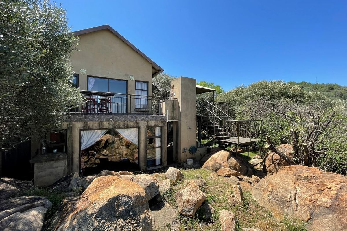 Rear view of the property featuring a balcony, external metal staircase, and sliding glass doors set against a natural rocky landscape.