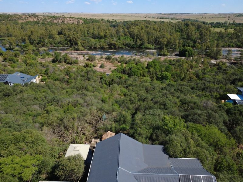 Aerial view of the property showcasing the metal roof, integrated solar panels, and expansive natural landscape with river frontage.