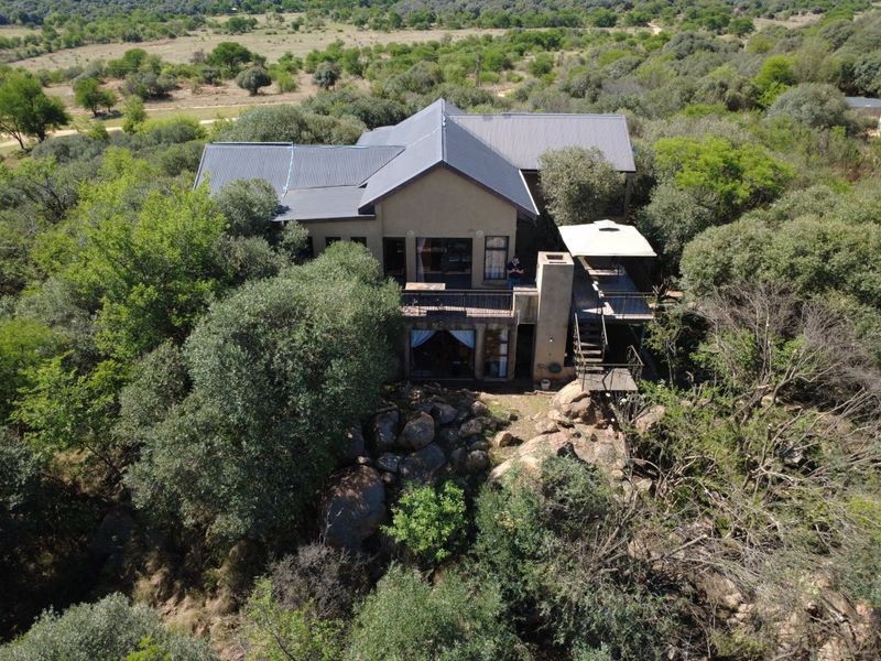 Aerial view of a multi-level small holding property featuring a metal roof, raised deck, and natural rocky landscape surroundings.