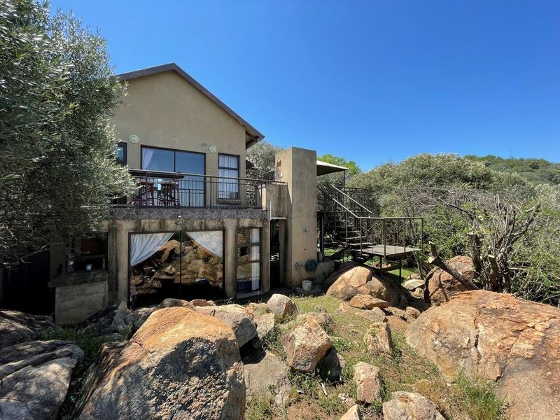 Rear view of the property featuring a balcony, external metal staircase, and sliding glass doors set against a natural rocky landscape.