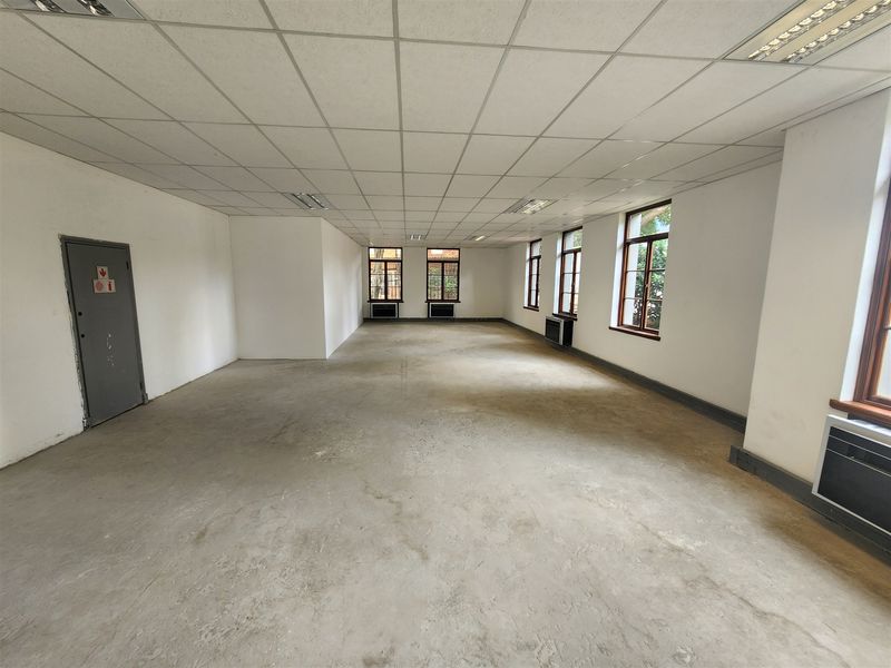 A spacious, vacant open-plan office area featuring a suspended ceiling, recessed lighting, and multiple windows providing natural light.