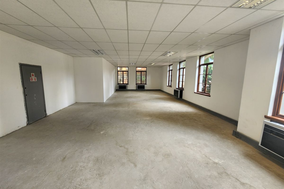 A spacious, vacant open-plan office area featuring a suspended ceiling, recessed lighting, and multiple windows providing natural light.