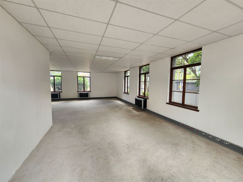 A spacious, vacant open-plan office area featuring a suspended ceiling, multiple windows, and integrated air conditioning units.
