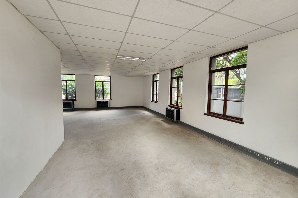 A spacious, vacant open-plan office area featuring a suspended ceiling, multiple windows, and integrated air conditioning units.