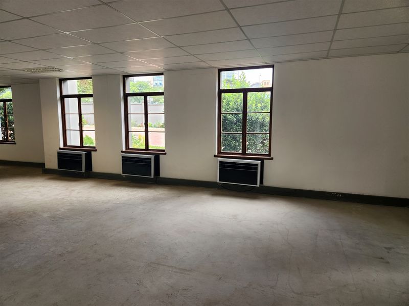 An empty, open-plan office space featuring suspended ceilings, concrete flooring, and multiple window-mounted air conditioning units.