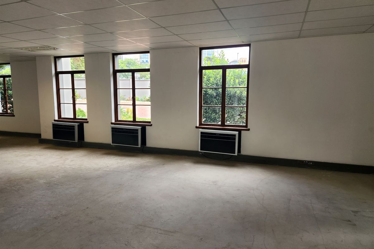 An empty, open-plan office space featuring suspended ceilings, concrete flooring, and multiple window-mounted air conditioning units.