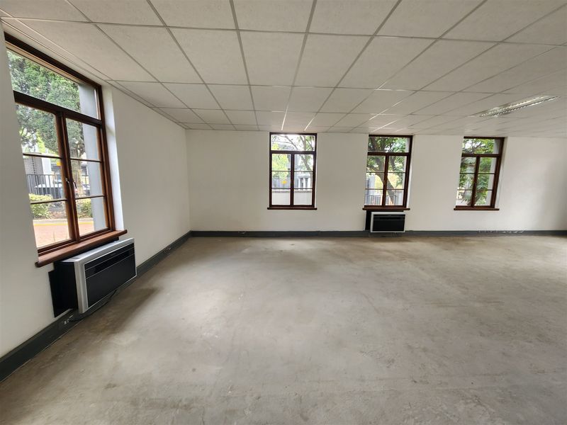 An empty, open-plan office space featuring a suspended ceiling, multiple timber-framed windows, and wall-mounted air conditioning units.