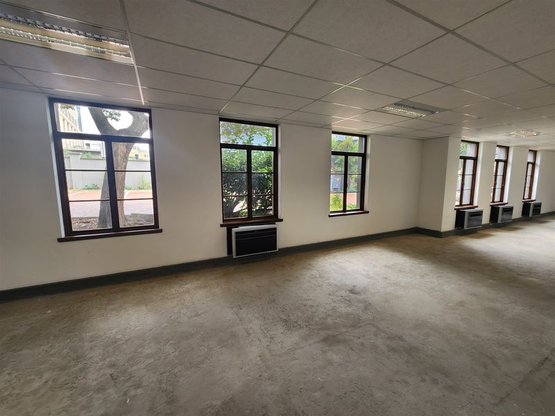 An empty office space featuring a suspended ceiling, recessed lighting, multiple windows with timber frames, and wall-mounted air conditioning units.